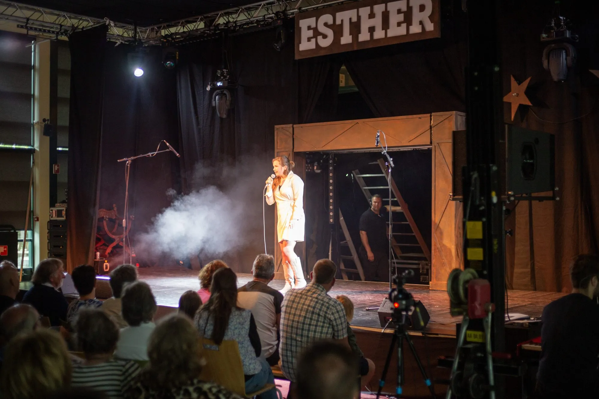 Een solist in een spot met rook op het decor van Esther