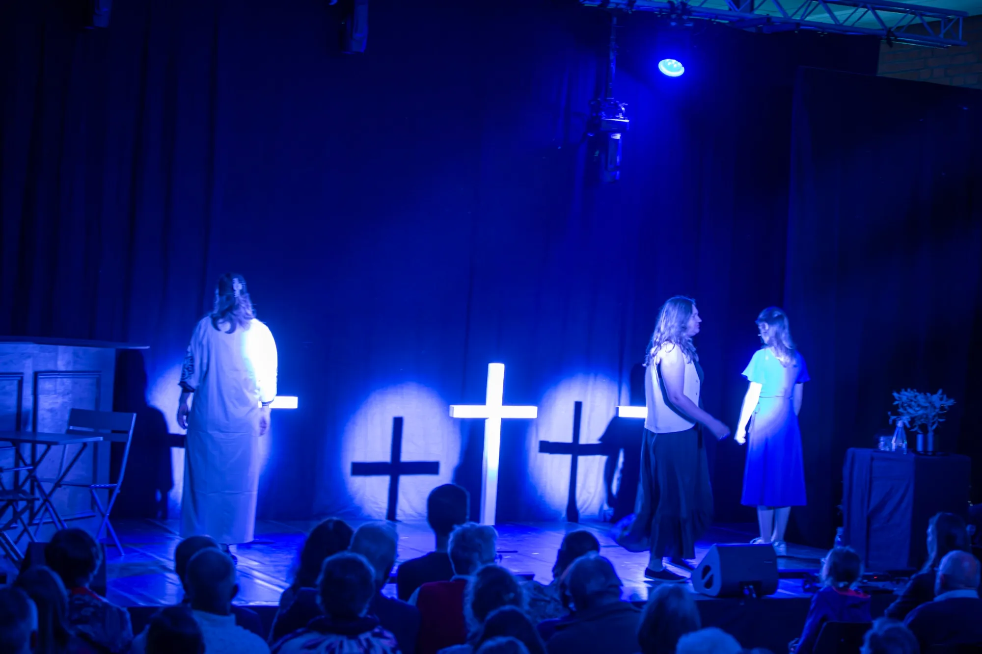 Drie lichtende kruizen in blauw licht, met de vrouwen aan weerszijden