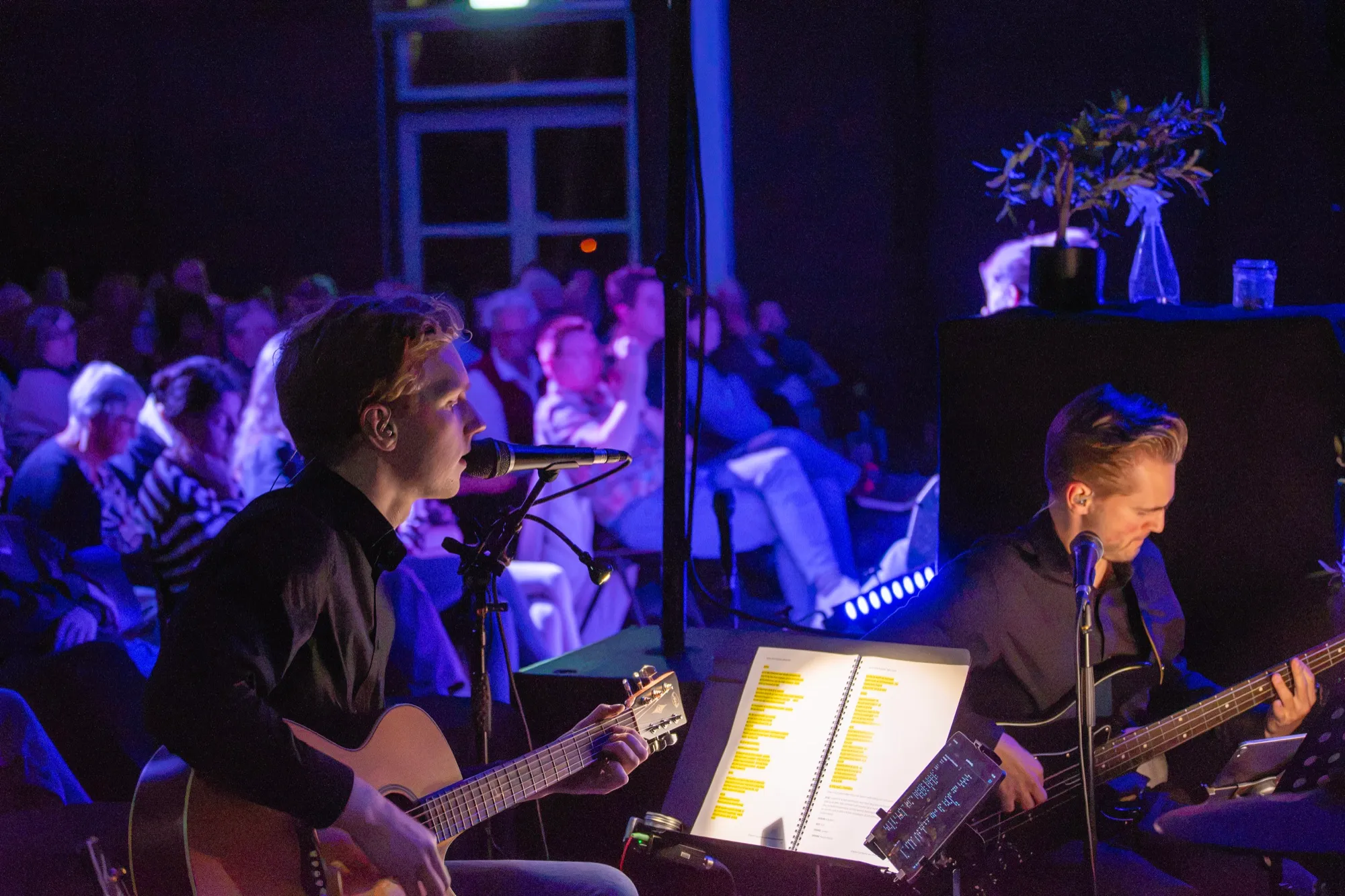 De musicalband speelt live naast het podium, met gitaar en toetsen